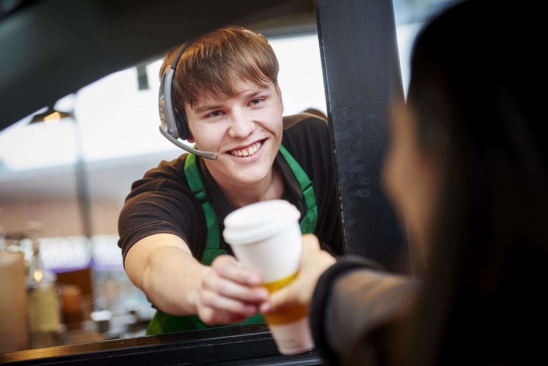 Barista at Welcome Break smiles and hands a coffee to a driver at a drive-through