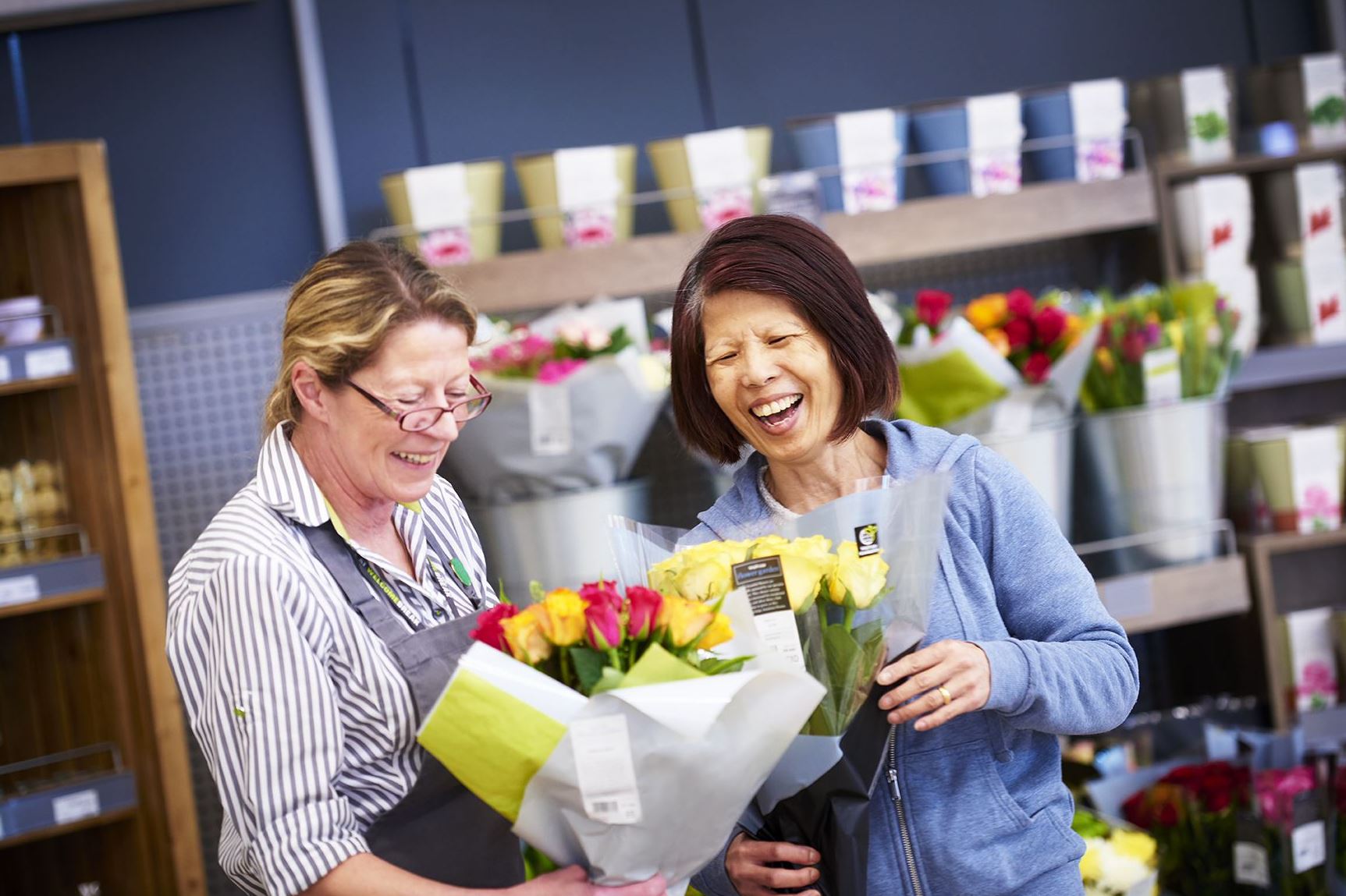Sales Assistant laughs with a customer as they look at a bouquet of bright flowers