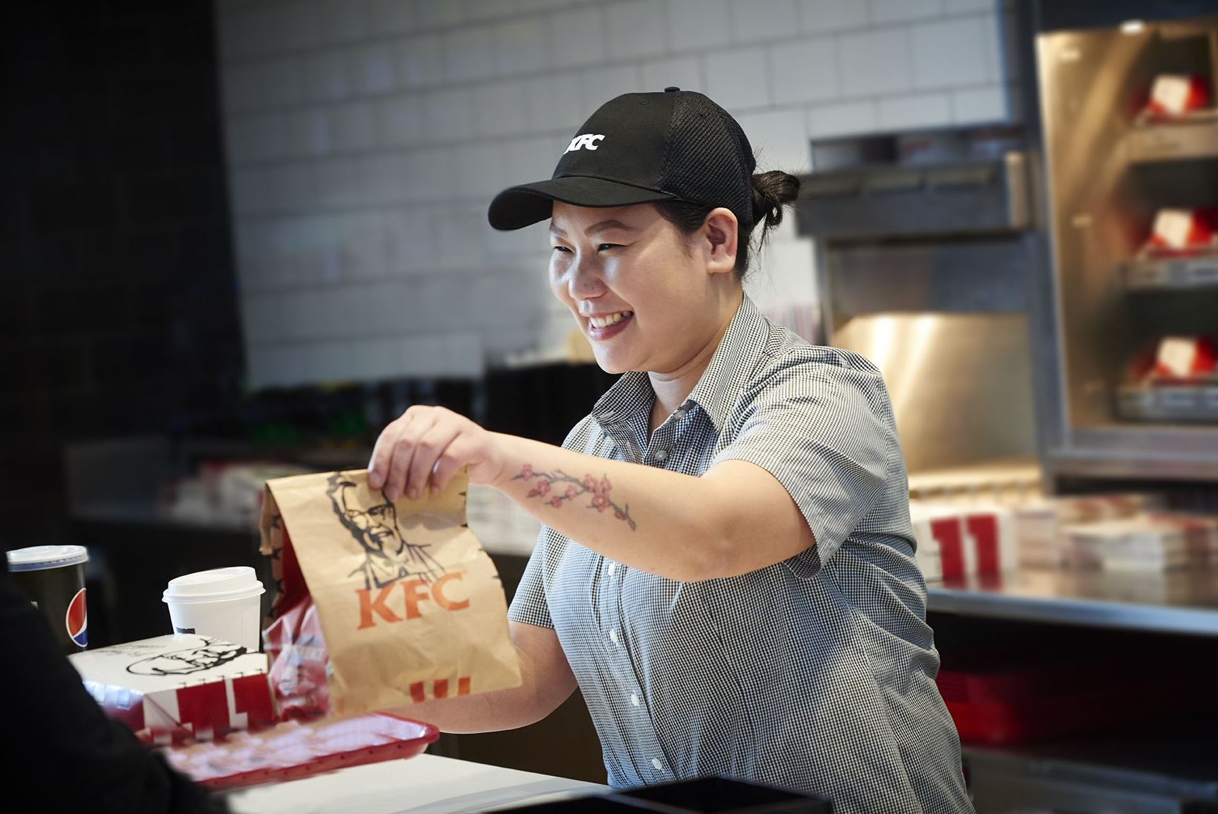 Team Member in KFC uniform at Welcome Break smiles as she offers a customer their order