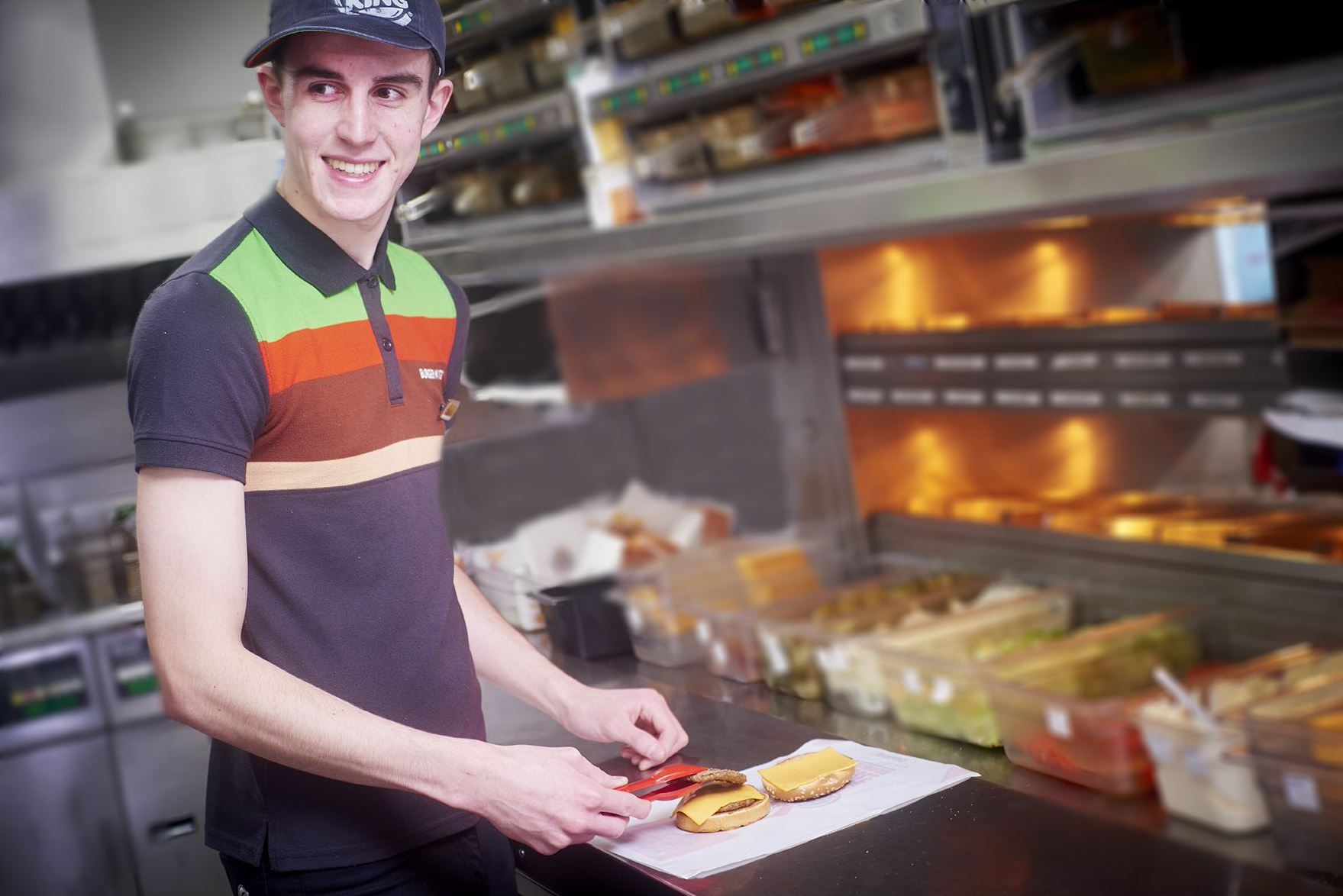 Kitchen Team Member in Burger King uniform at Welcome Break arranges a burger