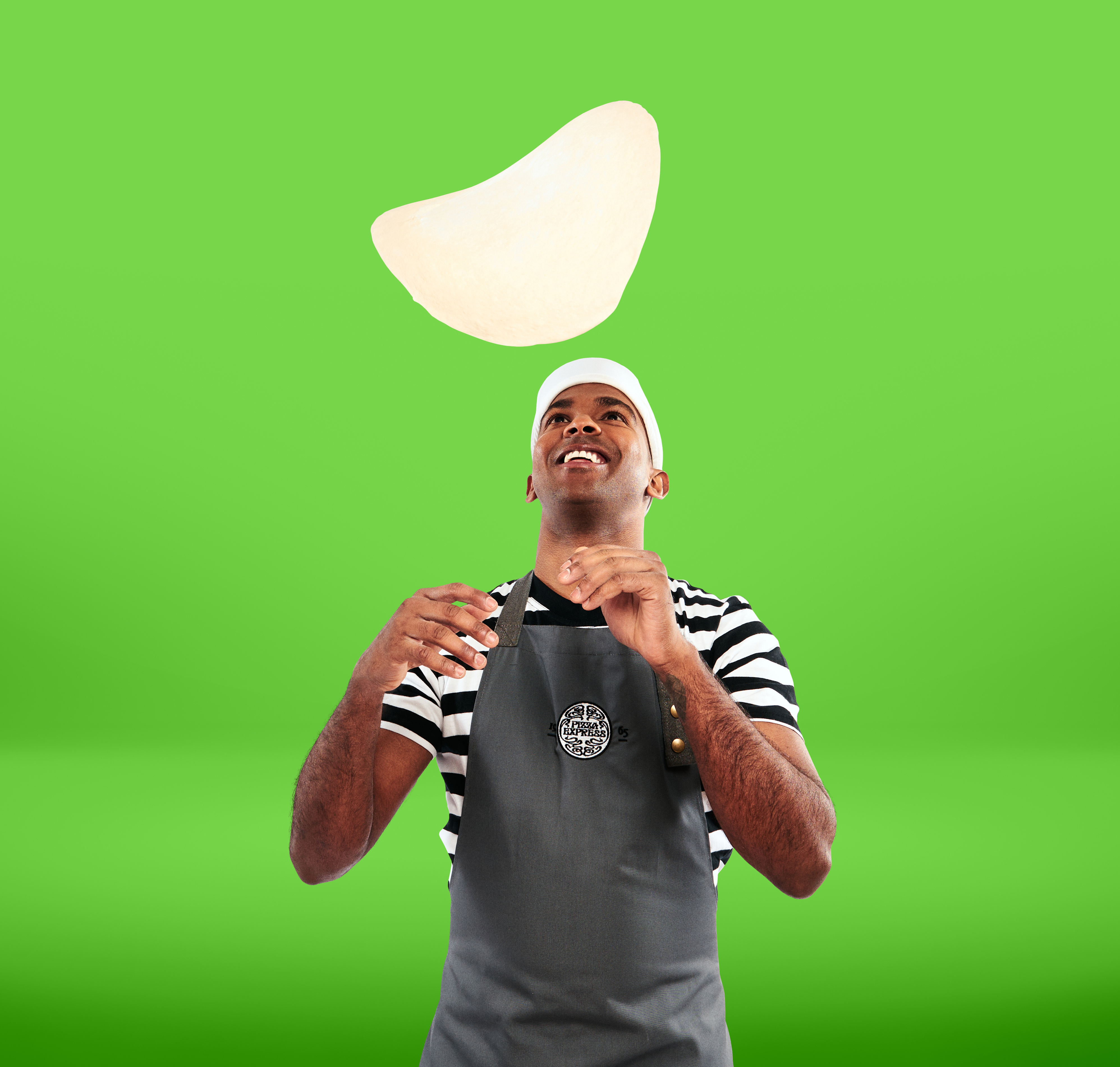 Elbis Avila from PizzaExpress tossing pizza in front of a light green background