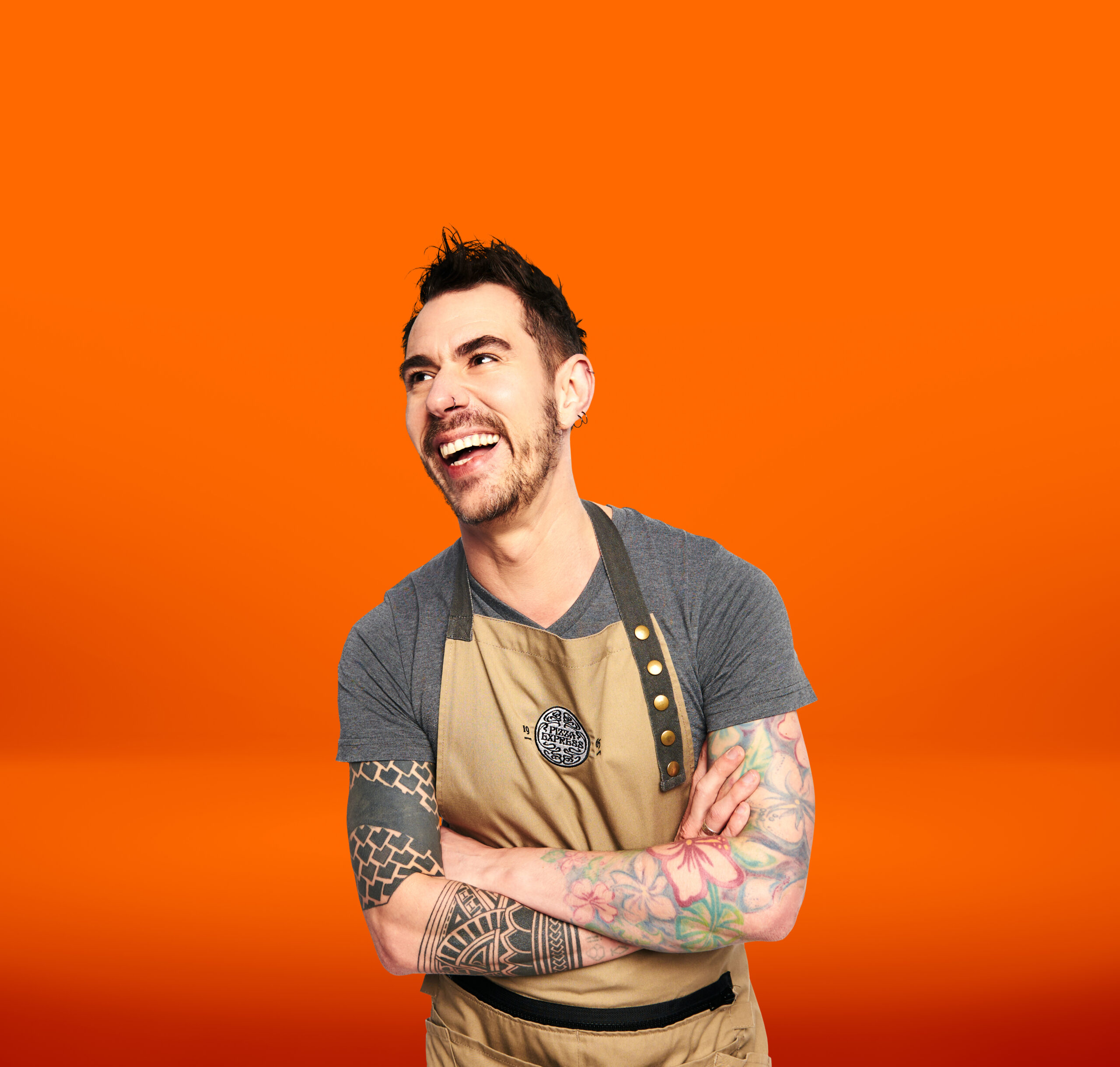 Stephen Santouris from PizzaEpxress grinning widely in front of orange background